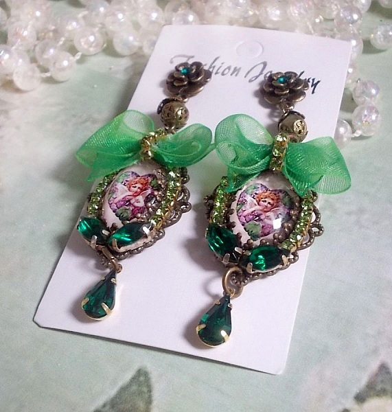 BO C&oelig;ur d&rsquo;Anges avec des cabochons d&rsquo;un petit ange orn&eacute;s d&rsquo;une cha&icirc;ne strass, navettes, poires et cabochons en Cristal. S&rsquo;ajoute des rubans organza sur pendentifs et clous en forme de fleurs.