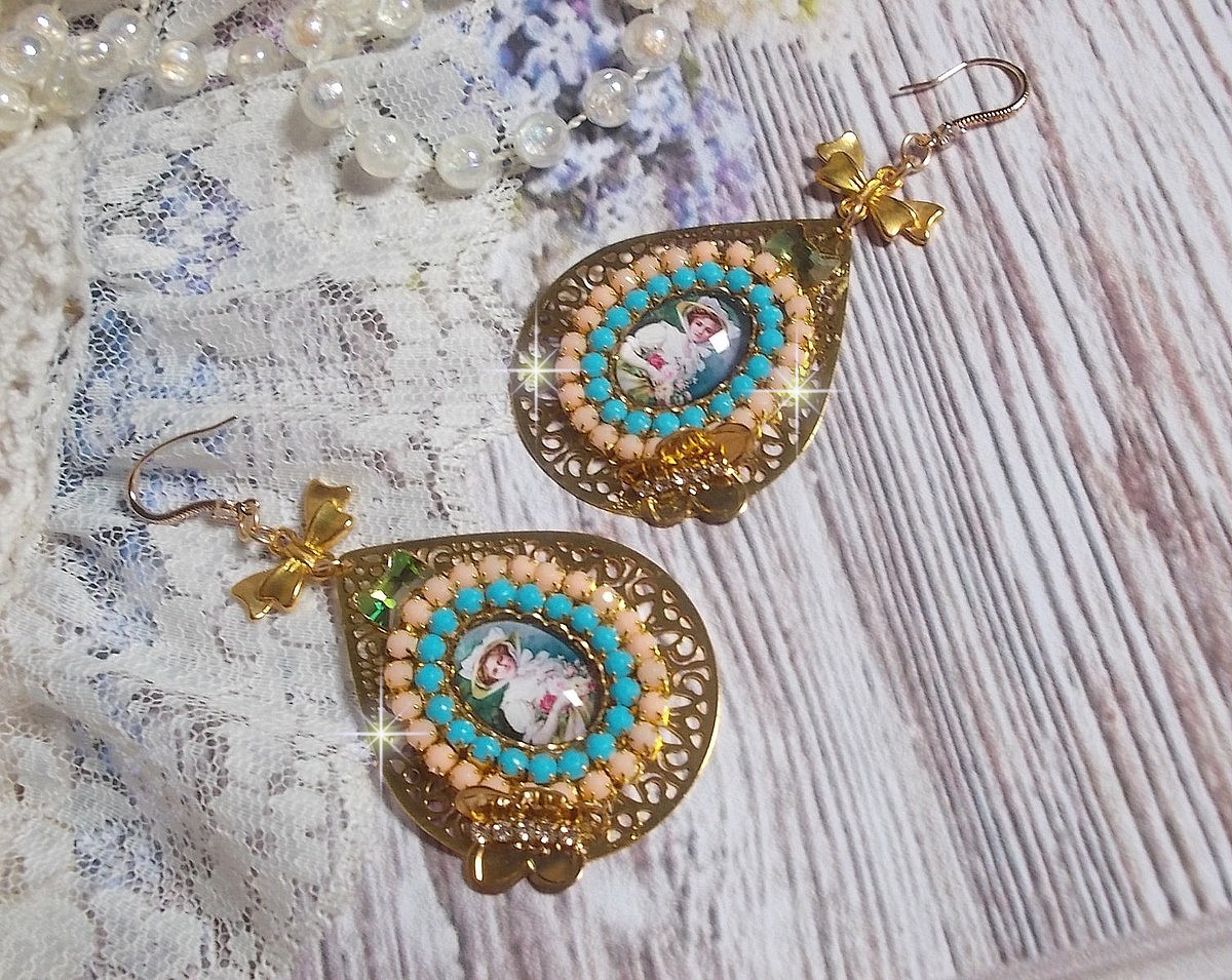 BO Mademoiselle Noellia avec des cabochons ovales repr&eacute;sentant une femme avec un chapeau et un n&oelig;ud blanc &agrave; laquelle s&rsquo;ajoute des cristaux, cha&icirc;nes strass P&ecirc;che et Turquoise sur crochets en plaqu&eacute; Or