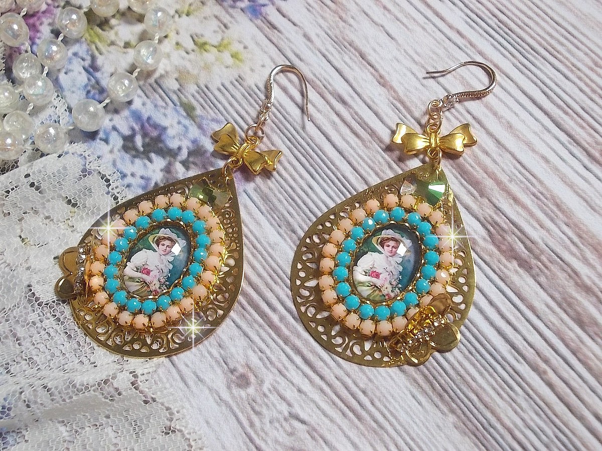 BO Mademoiselle Noellia avec des cabochons ovales repr&eacute;sentant une femme avec un chapeau et un n&oelig;ud blanc &agrave; laquelle s&rsquo;ajoute des cristaux, cha&icirc;nes strass P&ecirc;che et Turquoise sur crochets en plaqu&eacute; Or