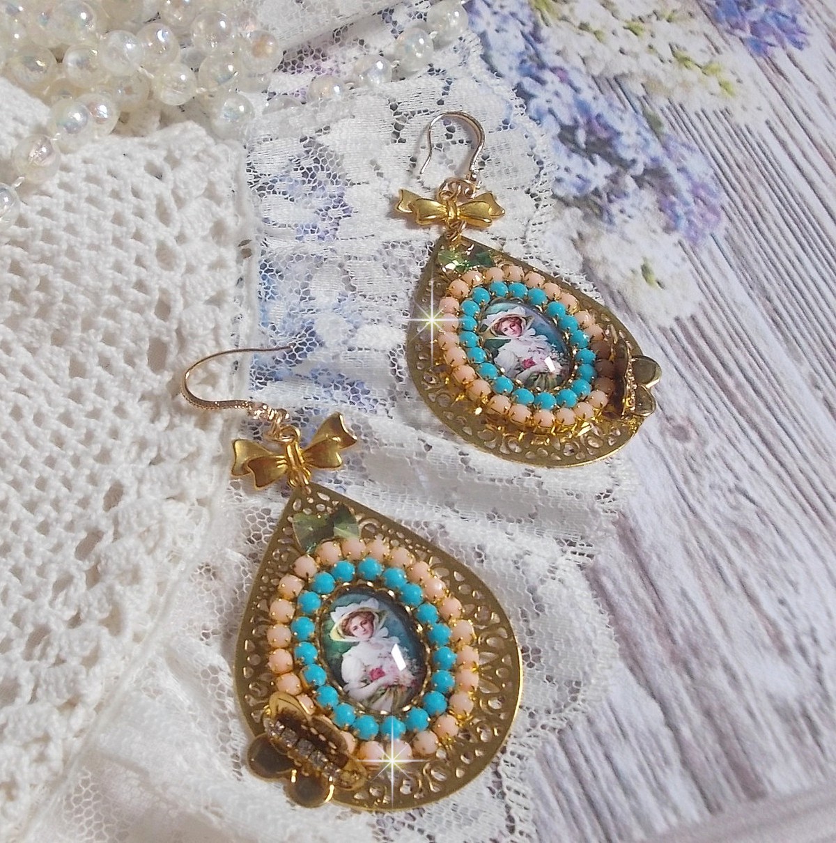 BO Mademoiselle Noellia avec des cabochons ovales repr&eacute;sentant une femme avec un chapeau et un n&oelig;ud blanc &agrave; laquelle s&rsquo;ajoute des cristaux, cha&icirc;nes strass P&ecirc;che et Turquoise sur crochets en plaqu&eacute; Or