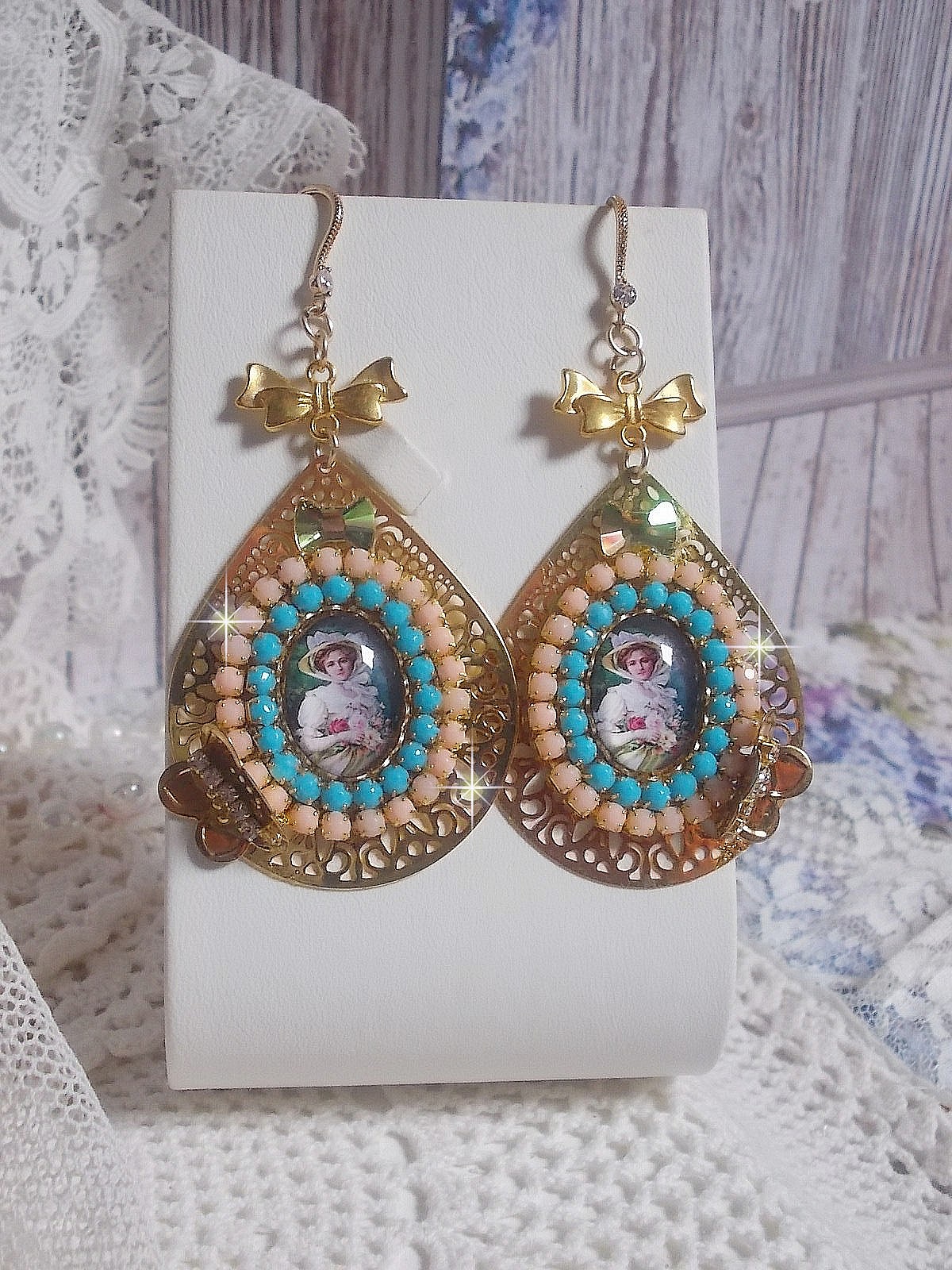 BO Mademoiselle Noellia avec des cabochons ovales repr&eacute;sentant une femme avec un chapeau et un n&oelig;ud blanc &agrave; laquelle s&rsquo;ajoute des cristaux, cha&icirc;nes strass P&ecirc;che et Turquoise sur crochets en plaqu&eacute; Or