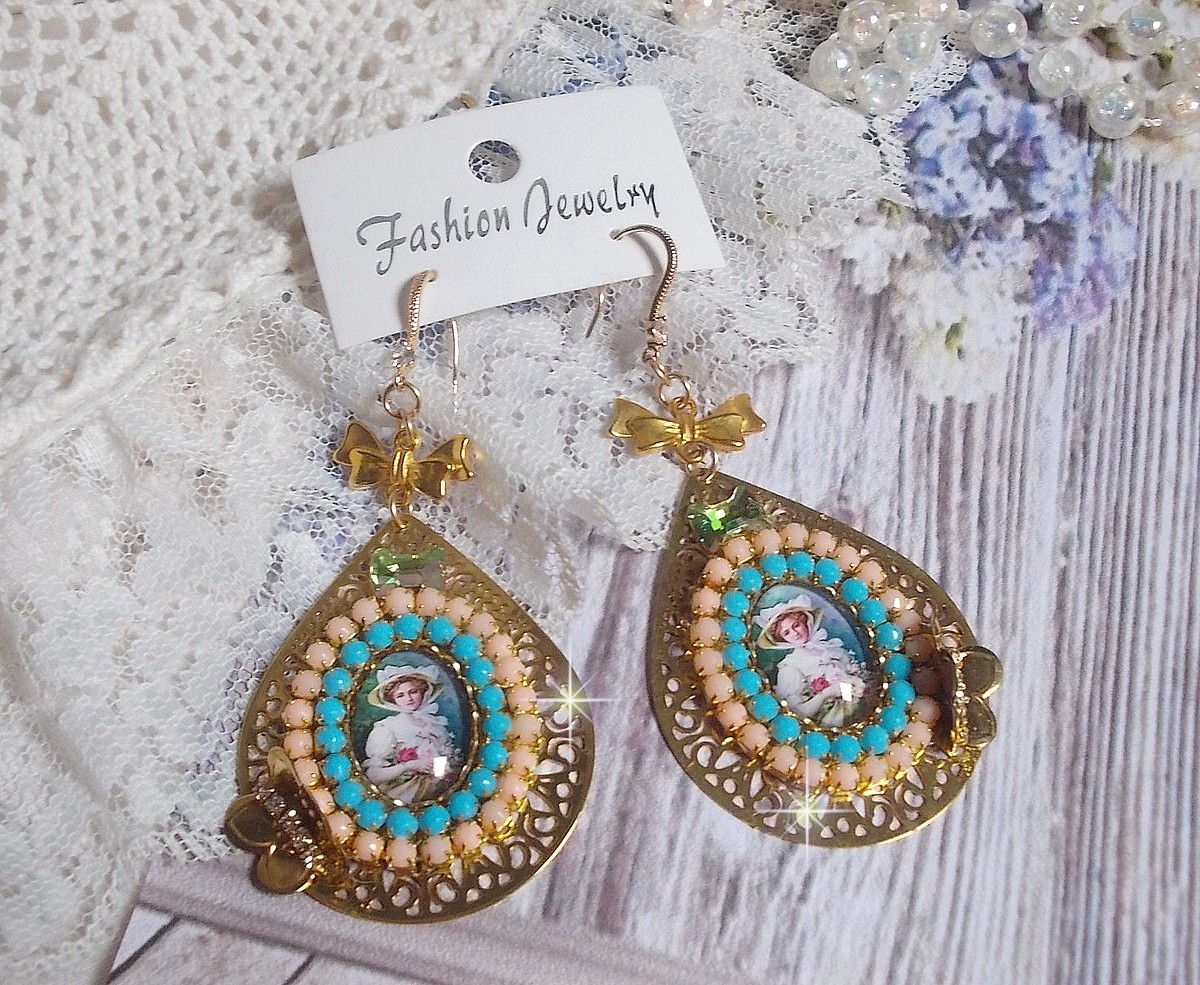 BO Mademoiselle Noellia avec des cabochons ovales repr&eacute;sentant une femme avec un chapeau et un n&oelig;ud blanc &agrave; laquelle s&rsquo;ajoute des cristaux, cha&icirc;nes strass P&ecirc;che et Turquoise sur crochets en plaqu&eacute; Or