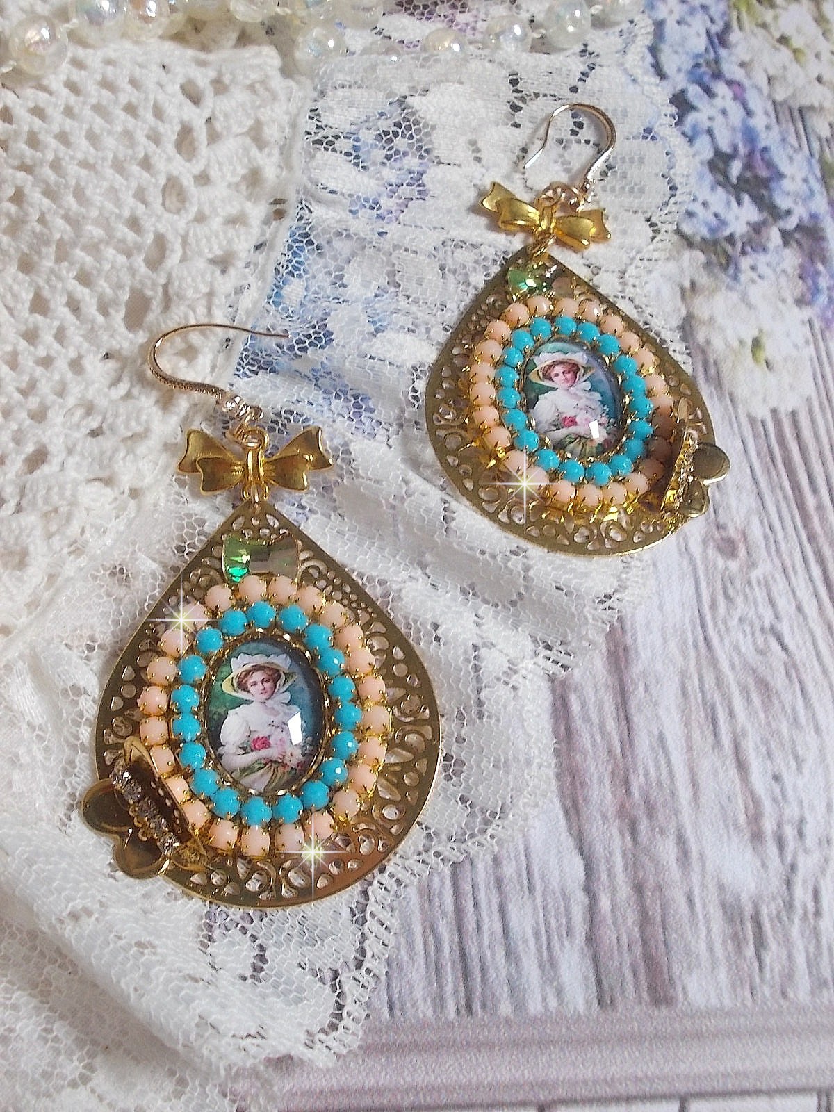 BO Mademoiselle Noellia avec des cabochons ovales repr&eacute;sentant une femme avec un chapeau et un n&oelig;ud blanc &agrave; laquelle s&rsquo;ajoute des cristaux, cha&icirc;nes strass P&ecirc;che et Turquoise sur crochets en plaqu&eacute; Or