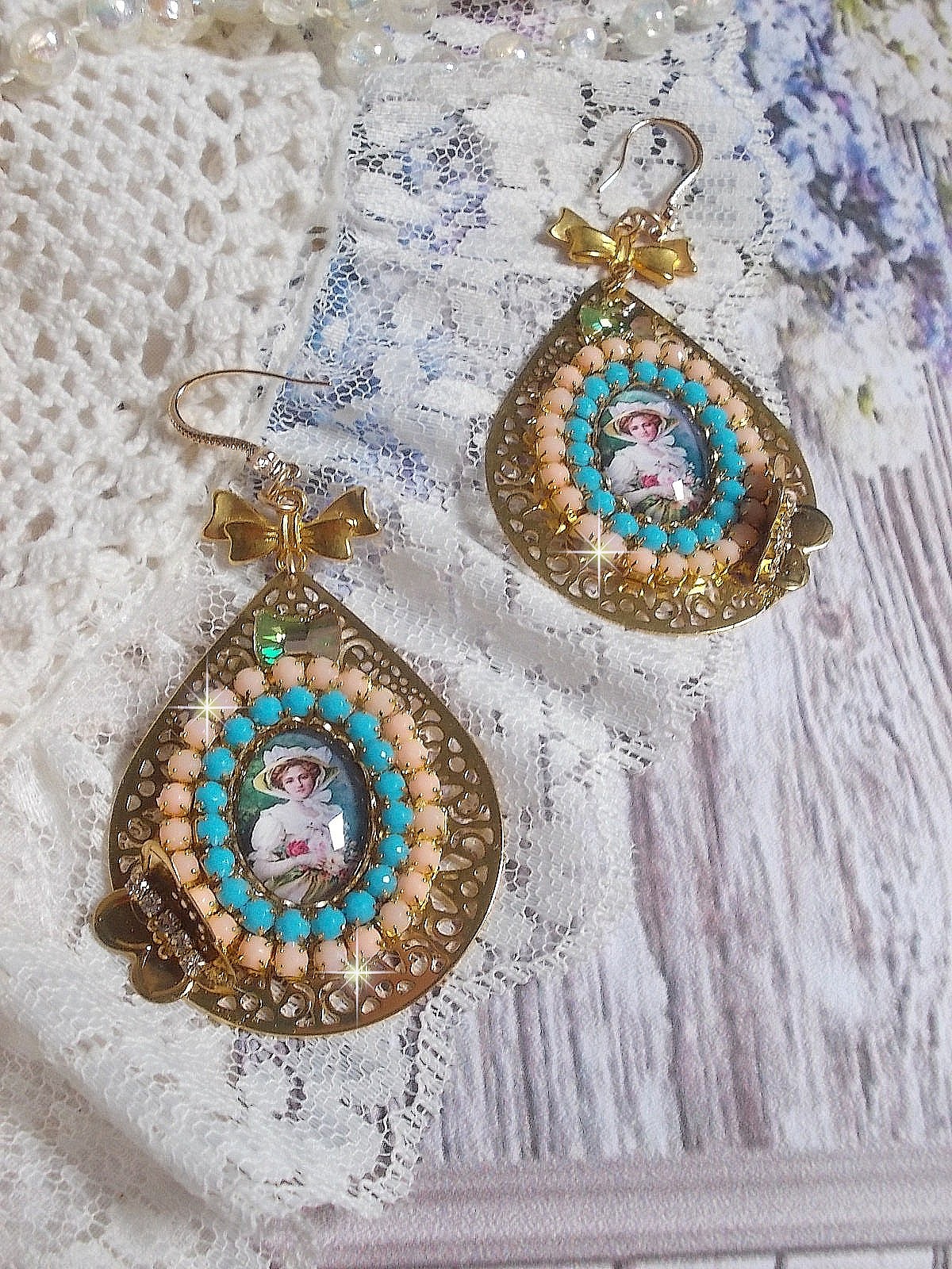 BO Mademoiselle Noellia avec des cabochons ovales repr&eacute;sentant une femme avec un chapeau et un n&oelig;ud blanc &agrave; laquelle s&rsquo;ajoute des cristaux, cha&icirc;nes strass P&ecirc;che et Turquoise sur crochets en plaqu&eacute; Or