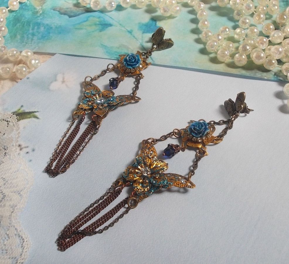 BO Papillons Iris&eacute;s mont&eacute;s sur estampes paillet&eacute;es de Bleu et Bronze, cabochons en forme de rose &agrave; laquelle s&rsquo;ajoute : coupelles fleurs, cha&icirc;ne strass, Zirconiums Cristal et gouttes Cobalt