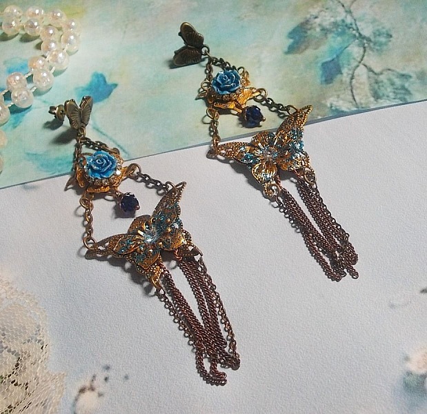 BO Papillons Iris&eacute;s mont&eacute;s sur estampes paillet&eacute;es de Bleu et Bronze, cabochons en forme de rose &agrave; laquelle s&rsquo;ajoute : coupelles fleurs, cha&icirc;ne strass, Zirconiums Cristal et gouttes Cobalt