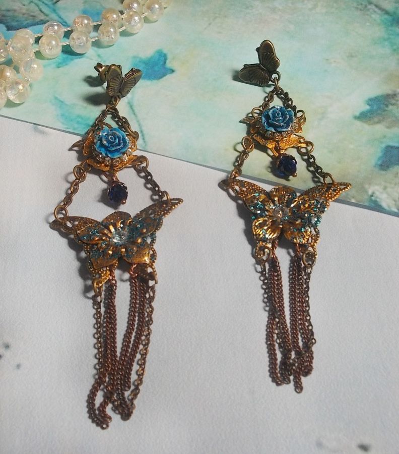 BO Papillons Iris&eacute;s mont&eacute;s sur estampes paillet&eacute;es de Bleu et Bronze, cabochons en forme de rose &agrave; laquelle s&rsquo;ajoute : coupelles fleurs, cha&icirc;ne strass, Zirconiums Cristal et gouttes Cobalt