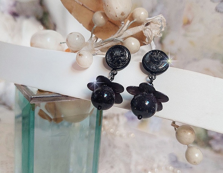 Boucles d'oreilles pendantes noires avec fleurs et perles scintillantes.