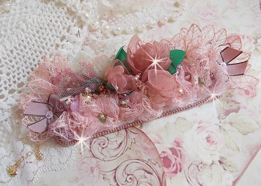 Bracelet Douceur Poudr&eacute;e manchette brod&eacute; avec une dentelle motif floral, ruban organza, tulles, n&oelig;uds, &eacute;tamines, sequins paillettes. La couleur dominante est le Rose &agrave; laquelle s&rsquo;ajoute des cristaux 