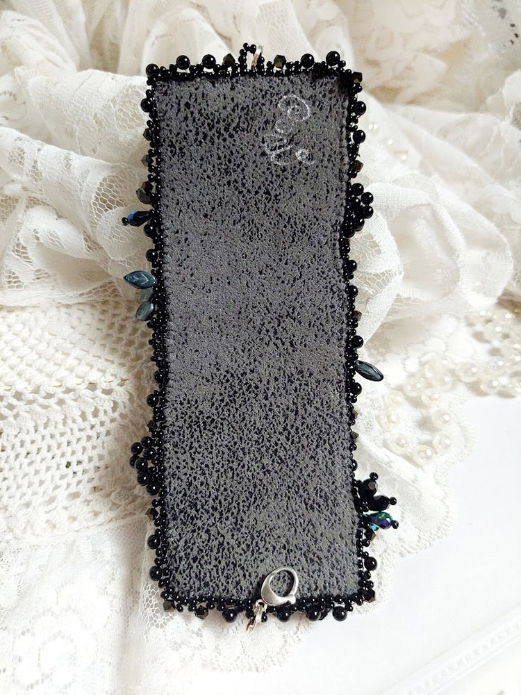 Bracelet manchette brodé noir sur fond de dentelle blanche.