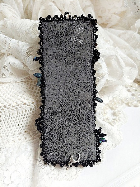 Bracelet manchette brodé noir sur fond de dentelle blanche.