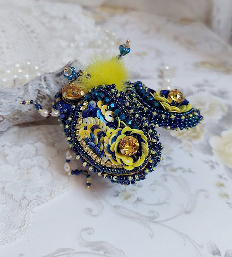 Broche artisanale en forme d'insecte bleu et jaune brodé.