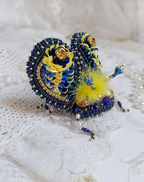Broche artisanale en forme d'insecte bleu et jaune brodé.