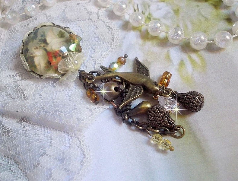 Broche Colombes aux plumages blancs avec des breloques filigran&eacute;es gouttes et lisses, perles rondes et n&oelig;ud en cristal, ruban organza cr&egrave;me, pendentif plaqu&eacute; or avec un zircon sur une broche en m&eacute;tal