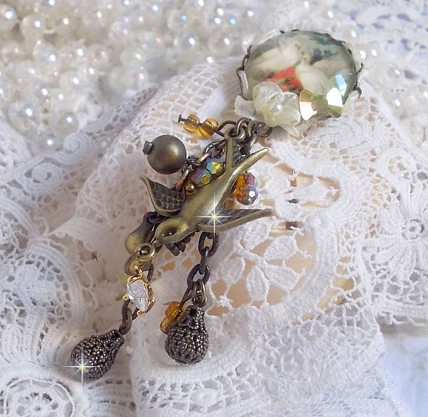 Broche Colombes aux plumages blancs avec des breloques filigran&eacute;es gouttes et lisses, perles rondes et n&oelig;ud en cristal, ruban organza cr&egrave;me, pendentif plaqu&eacute; or avec un zircon sur une broche en m&eacute;tal