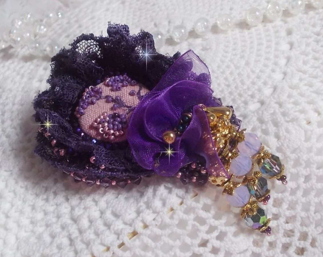 Broche Lady Romantique brod&eacute;e avec une dentelle violine ann&eacute;e 1950 avec un tissu en lin vieux rose brod&eacute; de fleurs et branches en rocailles bord&eacute; d&rsquo;un ruban organza, fleurs, cristaux et breloques