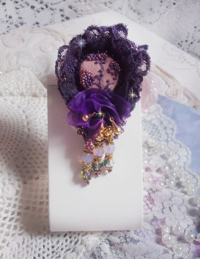 Broche Lady Romantique brod&eacute;e avec une dentelle violine ann&eacute;e 1950 avec un tissu en lin vieux rose brod&eacute; de fleurs et branches en rocailles bord&eacute; d&rsquo;un ruban organza, fleurs, cristaux et breloques
