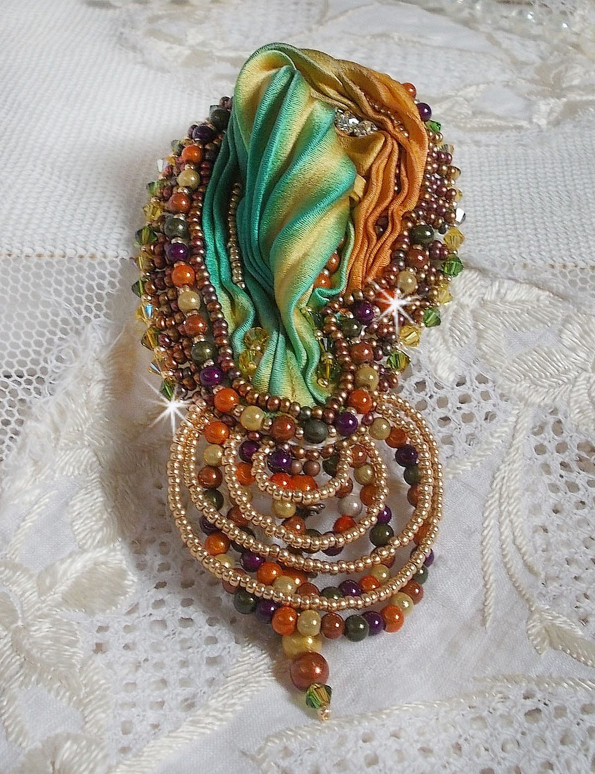Broche Lune V&eacute;nitienne brod&eacute;e avec un ruban de soie orange, vert et jaune, cristaux, : toupies et chatons. S&rsquo;ajoute &agrave; l&rsquo;ensemble des perles magiques et rocailles sur une broche Dor&eacute; 