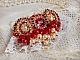 Broche Rubis brod&eacute;e avec trois cabochons Ivoire et Rouge &agrave; laquelle s&rsquo;ajoute des toupies aux couleurs Cristal, Burgundy et Garnet, des perles nacr&eacute;es et opaque. Mont&eacute; sur une dentelle et une broche