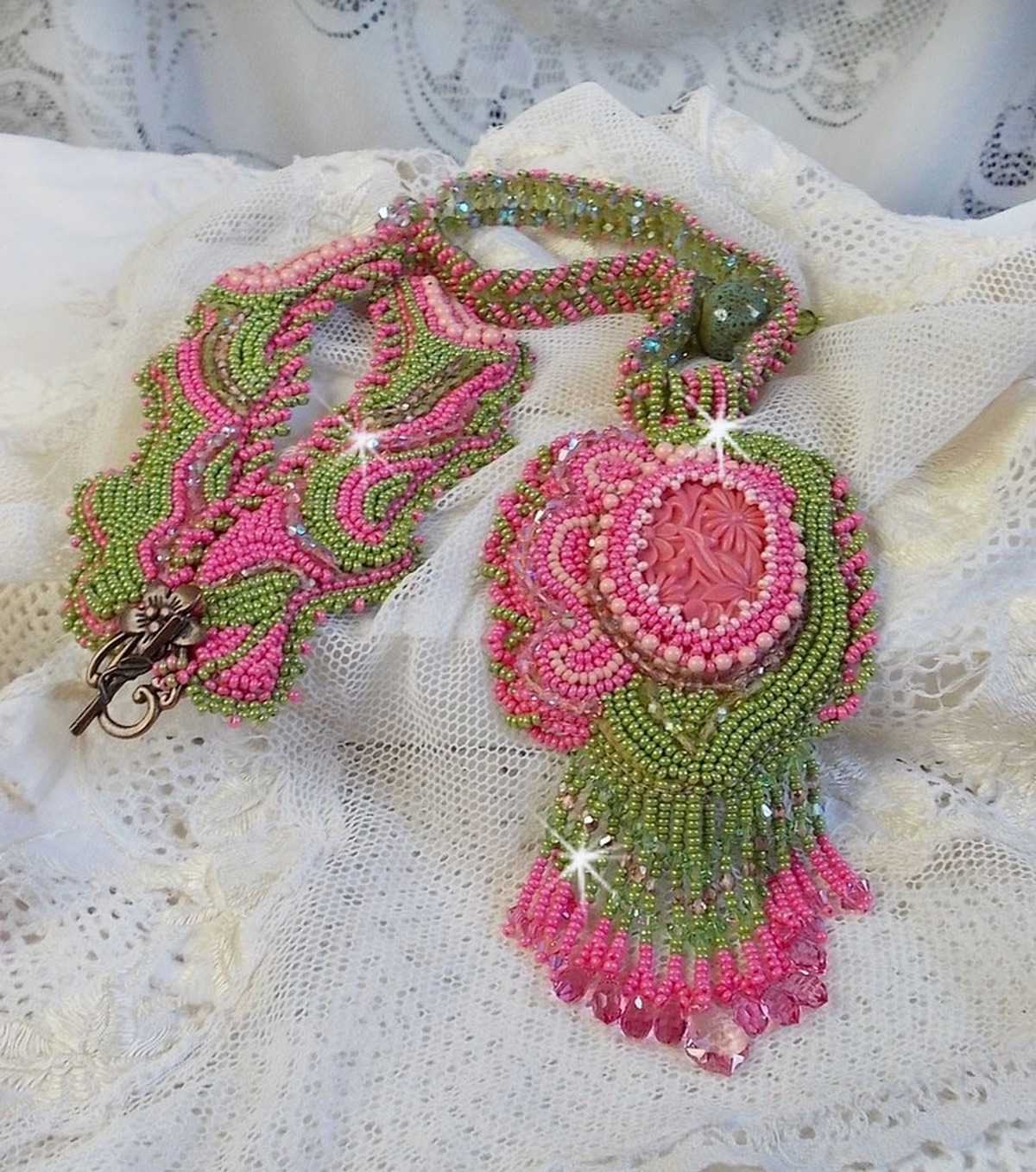 Collier Miss Lady brod&eacute; avec un cabochon repr&eacute;sentant des fleurs de couleur Rose Pink &agrave; laquelle s'ajoute perles rondes, toupies en Cristal, facettes, rocailles Anis, Rose et perle c&eacute;ramique 