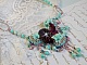 Collier Blue Flowers brod&eacute; avec un ruban de soie framboise/truffe &agrave; laquelle s&rsquo;ajoute : cabochons, perles nacr&eacute;es Rosaline et Ivoire, toupies Jet, anneaux ovales, perles marbr&eacute;es Bleu Ciel et Blanc