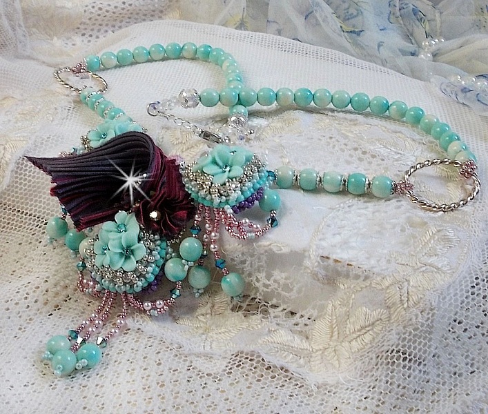 Collier Blue Flowers brod&eacute; avec un ruban de soie framboise/truffe &agrave; laquelle s&rsquo;ajoute : cabochons, perles nacr&eacute;es Rosaline et Ivoire, toupies Jet, anneaux ovales, perles marbr&eacute;es Bleu Ciel et Blanc