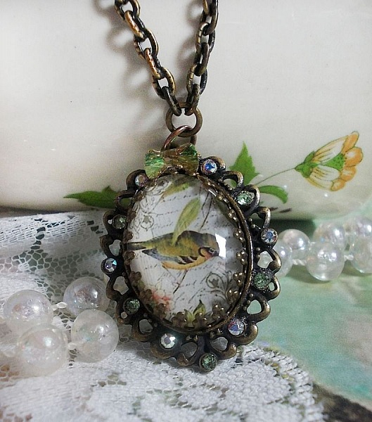 Collier Oiseau des Jardins s&rsquo;inspire d&rsquo;un oiseau dans la nature. Sur une base d&rsquo;un pendentif, ce motif est orn&eacute; de cristaux : n&oelig;ud et cabochons aux nuances cristal et P&eacute;ridot. Mont&eacute; sur cha&icirc;ne Laiton