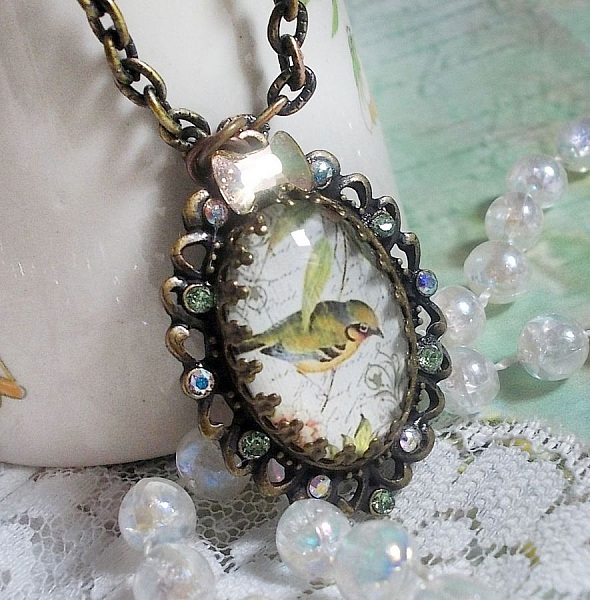 Collier Oiseau des Jardins s&rsquo;inspire d&rsquo;un oiseau dans la nature. Sur une base d&rsquo;un pendentif, ce motif est orn&eacute; de cristaux : n&oelig;ud et cabochons aux nuances cristal et P&eacute;ridot. Mont&eacute; sur cha&icirc;ne Laiton