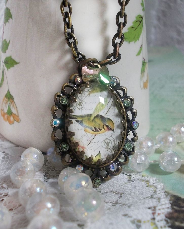 Collier Oiseau des Jardins s&rsquo;inspire d&rsquo;un oiseau dans la nature. Sur une base d&rsquo;un pendentif, ce motif est orn&eacute; de cristaux : n&oelig;ud et cabochons aux nuances cristal et P&eacute;ridot. Mont&eacute; sur cha&icirc;ne Laiton