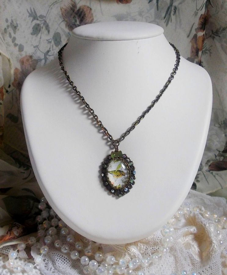 Collier Oiseau des Jardins s&rsquo;inspire d&rsquo;un oiseau dans la nature. Sur une base d&rsquo;un pendentif, ce motif est orn&eacute; de cristaux : n&oelig;ud et cabochons aux nuances cristal et P&eacute;ridot. Mont&eacute; sur cha&icirc;ne Laiton