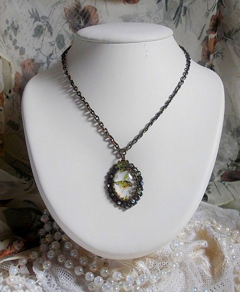 Collier Oiseau des Jardins s&rsquo;inspire d&rsquo;un oiseau dans la nature. Sur une base d&rsquo;un pendentif, ce motif est orn&eacute; de cristaux : n&oelig;ud et cabochons aux nuances cristal et P&eacute;ridot. Mont&eacute; sur cha&icirc;ne Laiton