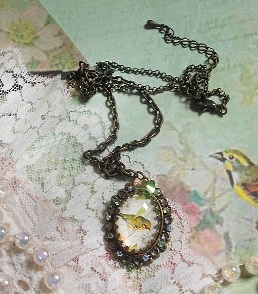 Collier Oiseau des Jardins s&rsquo;inspire d&rsquo;un oiseau dans la nature. Sur une base d&rsquo;un pendentif, ce motif est orn&eacute; de cristaux : n&oelig;ud et cabochons aux nuances cristal et P&eacute;ridot. Mont&eacute; sur cha&icirc;ne Laiton
