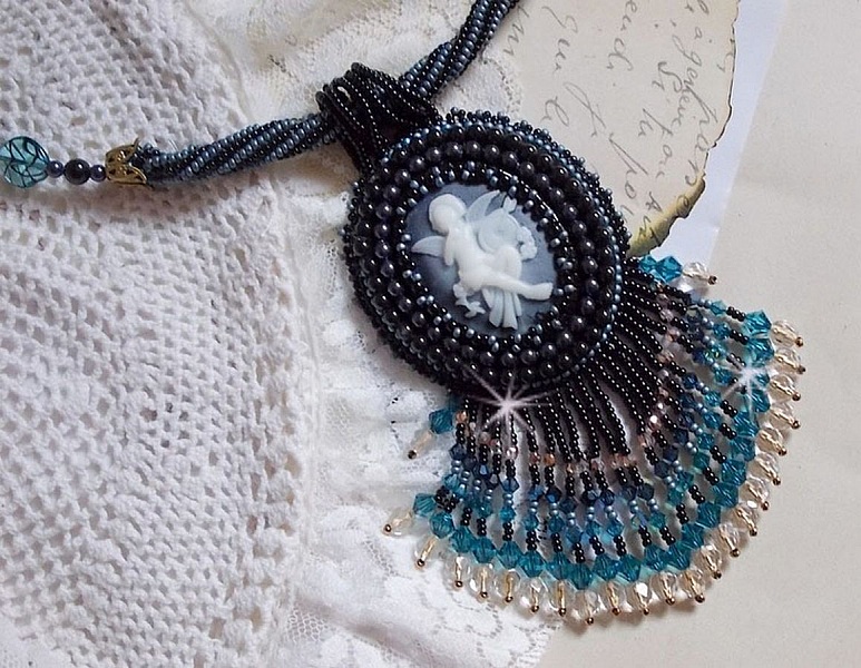 Pendentif Angelot avec un cabochon Ange brod&eacute; de perles rondes nacr&eacute;es Cristal avec des rocailles. S&rsquo;ajoute des facettes, toupies, perles ovales Lampwok serti d&rsquo;un ruban Dor&eacute; et palets