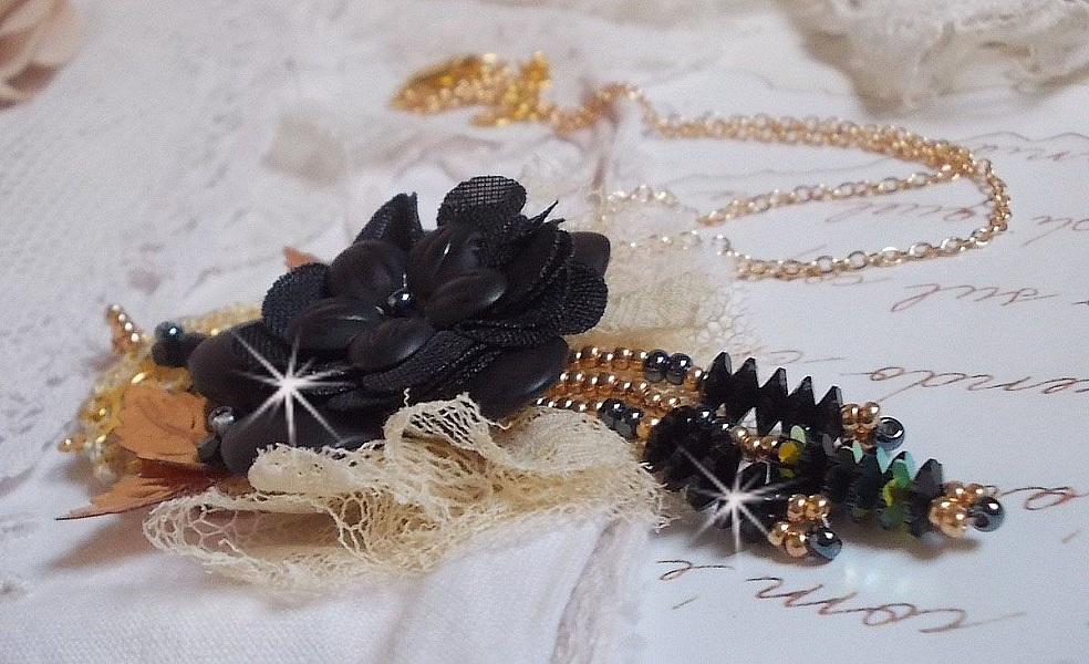 Pendentif Attrapes R&ecirc;ves brod&eacute; avec des fleurs Lucites Noires sur une dentelle Beige et une estampe dor&eacute;e. Les pendants sont des fleurs en cristal avec des rocailles. Mont&eacute; avec une cha&icirc;ne plaqu&eacute; Or