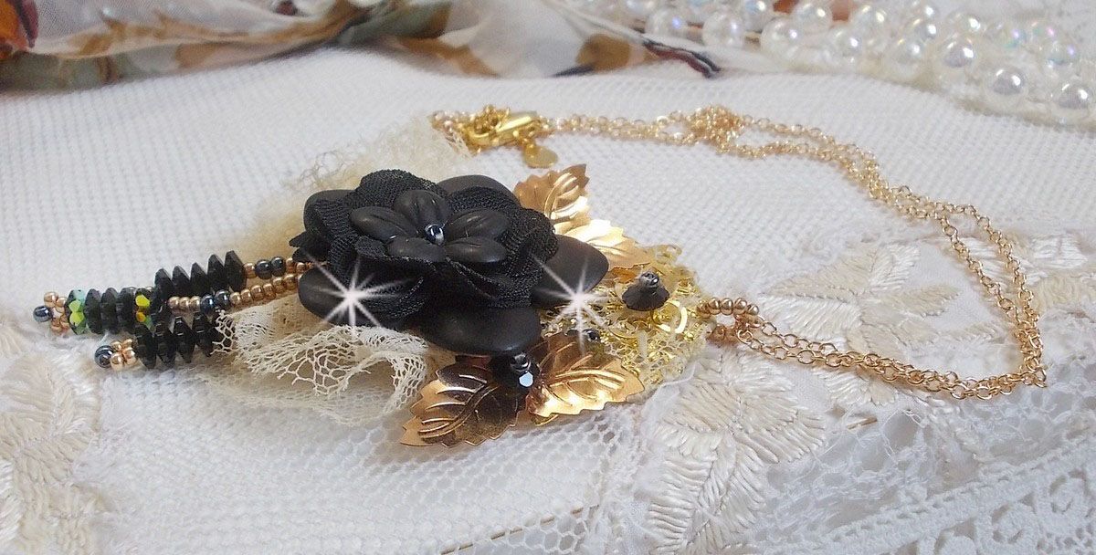 Pendentif Attrapes R&ecirc;ves brod&eacute; avec des fleurs Lucites Noires sur une dentelle Beige et une estampe dor&eacute;e. Les pendants sont des fleurs en cristal avec des rocailles. Mont&eacute; avec une cha&icirc;ne plaqu&eacute; Or