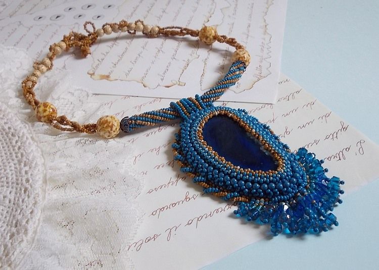 Pendentif Corsica avec un cabochon : une Agate Bleue brod&eacute;e avec des perles nacr&eacute;es Bleu Lapis en cristal &agrave; laquelle s&rsquo;ajoute des rocailles saphir et travertin entrelac&eacute;es pour former une dentelle