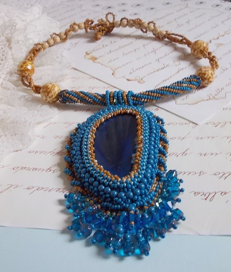Pendentif Corsica avec un cabochon : une Agate Bleue brod&eacute;e avec des perles nacr&eacute;es Bleu Lapis en cristal &agrave; laquelle s&rsquo;ajoute des rocailles saphir et travertin entrelac&eacute;es pour former une dentelle