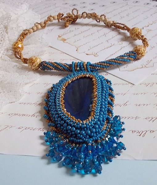 Pendentif Corsica avec un cabochon : une Agate Bleue brod&eacute;e avec des perles nacr&eacute;es Bleu Lapis en cristal &agrave; laquelle s&rsquo;ajoute des rocailles saphir et travertin entrelac&eacute;es pour former une dentelle