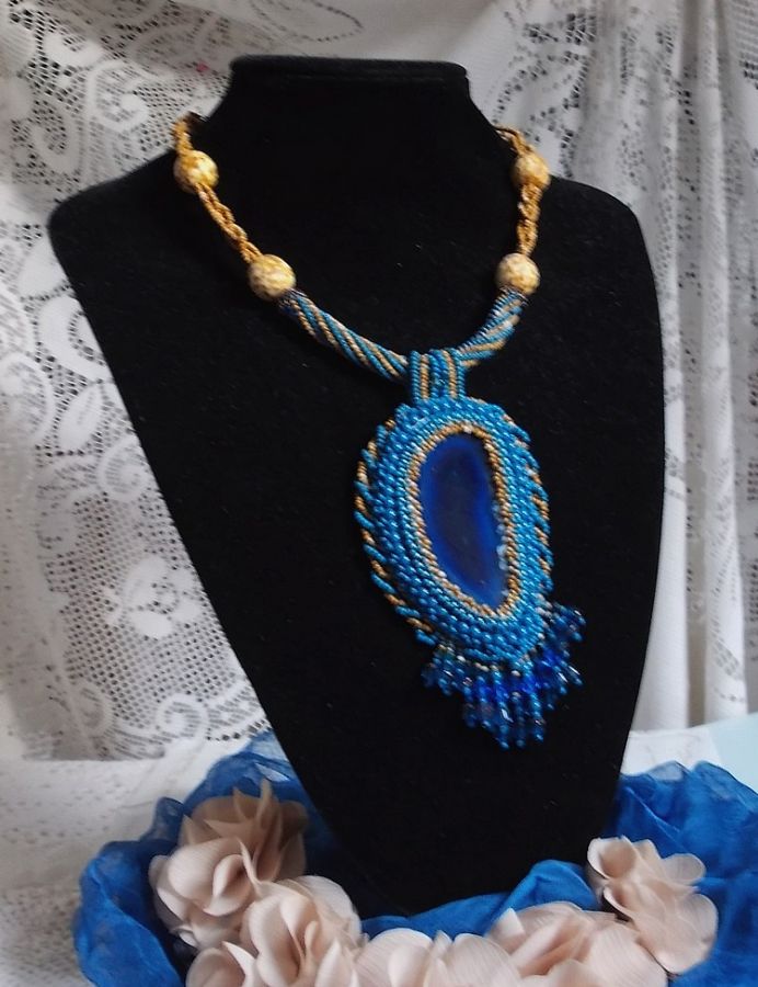 Pendentif Corsica avec un cabochon : une Agate Bleue brod&eacute;e avec des perles nacr&eacute;es Bleu Lapis en cristal &agrave; laquelle s&rsquo;ajoute des rocailles saphir et travertin entrelac&eacute;es pour former une dentelle