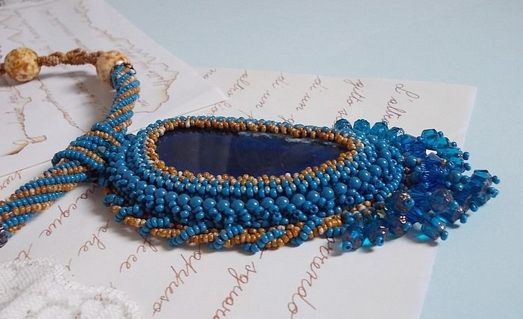 Pendentif Corsica avec un cabochon : une Agate Bleue brod&eacute;e avec des perles nacr&eacute;es Bleu Lapis en cristal &agrave; laquelle s&rsquo;ajoute des rocailles saphir et travertin entrelac&eacute;es pour former une dentelle