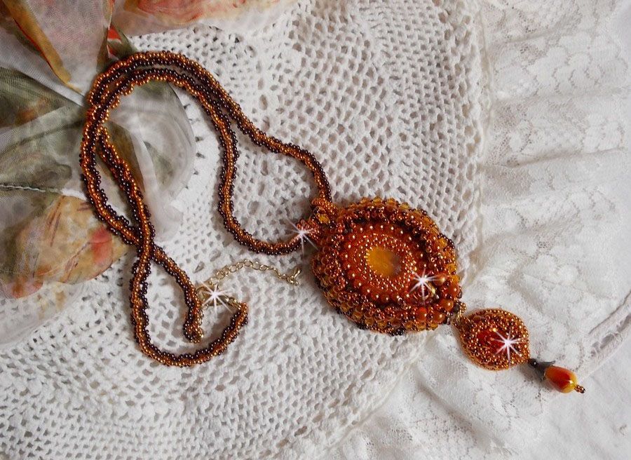 Pendentif artisanal brodé aux perles orange et tons dorés.