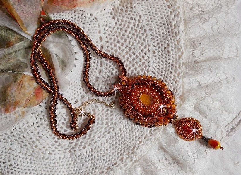 Pendentif artisanal brodé aux perles orange et tons dorés.