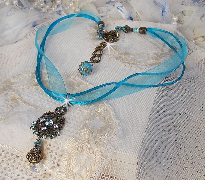 Pendentif Lady in Blue mont&eacute; avec des chandeliers, des cristaux : cabochons, perles rondes et toupies, perles en c&eacute;ramique, cabochons Zirconium, rocailles et rubans. Tout est de couleur Bleu et Bronze