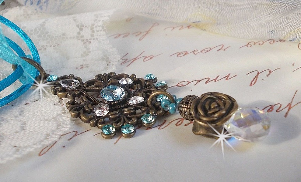 Pendentif Lady in Blue mont&eacute; avec des chandeliers, des cristaux : cabochons, perles rondes et toupies, perles en c&eacute;ramique, cabochons Zirconium, rocailles et rubans. Tout est de couleur Bleu et Bronze