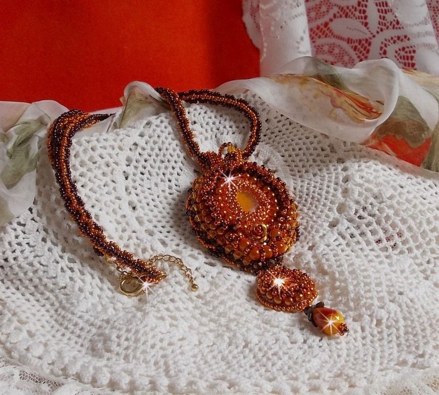 Pendentif artisanal brodé de perles orange et dorées.