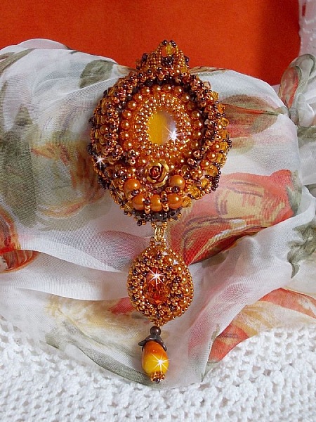 Pendentif artisanal brodé de perles orange et dorées.