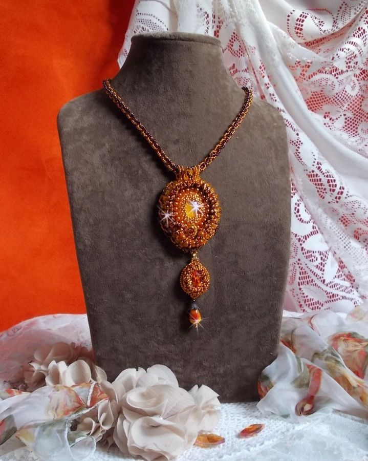 Pendentif artisanal brodé aux perles orange et tons dorés.