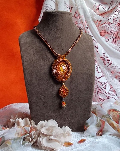 Pendentif artisanal brodé aux perles orange et tons dorés.
