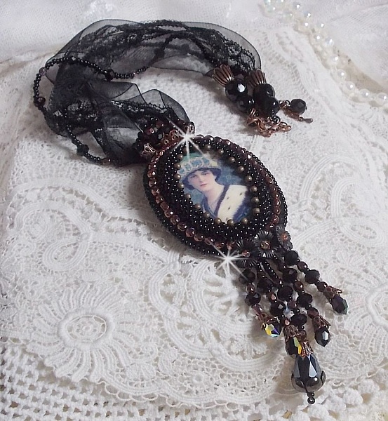 Pendentif Midnight Daisy avec un cabochon en bois repr&eacute;sentant une femme en chapeau Bleu, brod&eacute; avec des fleurs lucites, coupelles et facettes. Le tout est fini avec une dentelle Noire et un ruban