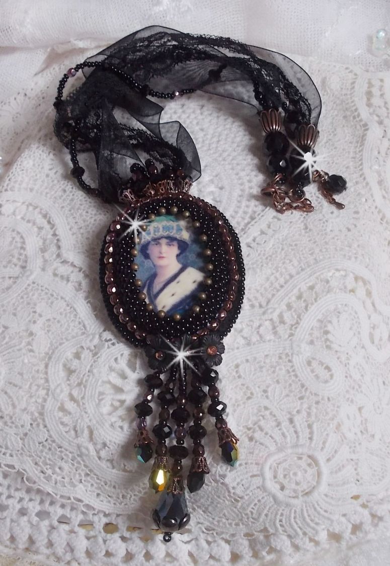 Pendentif Midnight Daisy avec un cabochon en bois repr&eacute;sentant une femme en chapeau Bleu, brod&eacute; avec des fleurs lucites, coupelles et facettes. Le tout est fini avec une dentelle Noire et un ruban